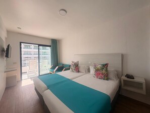 Ein Hotelzimmer mit einem großen Bett, einem Nachttisch, einem Sessel, Blick auf den Außenbalkon und einem an der Wand montierten Fernseher.