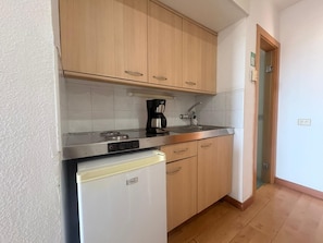Una cocina compacta con refrigerador, cafetera y armarios de madera.