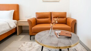 A modern hotel room with a bed, a sofa, a small table with a vase, and a framed picture on the wall.