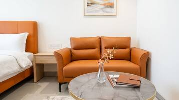 Ein modernes Hotelzimmer mit einem Bett, einer Couch, einem kleinen Tisch mit einer Vase und einem gerahmten Bild an der Wand.