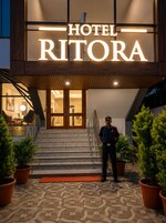 A hotel entrance with a sign reading 'HOTEL RITORA,' a security guard, and potted plants.
