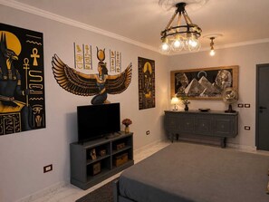 Ein Zimmer mit Flachbildfernseher, einer Kristallleuchter, einem Schrank und Wandbildern mit ägyptischen Motiven.