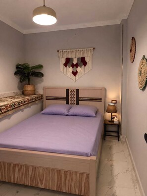 Ein Schlafzimmer mit einem Bett, einem Nachttisch mit Lampe, einer Wanddekoration und einem Topfpflanzen.