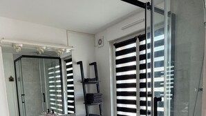 Een badkamer met een douchecabine van glas, een wit wastafelmeubel, een spiegel en een handdoekrek.