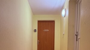 A hallway with a wooden door marked 'Bienvenue,' a light switch, and a doorbell on the wall.
