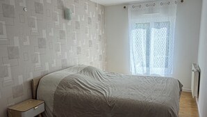 A bedroom with a bed, a nightstand, a radiator, and a window with a curtain.