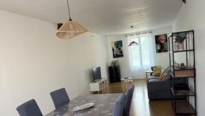 A dining area with a wooden table and chairs, a television, and a sofa in the background.