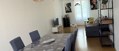 A dining area with a wooden table and chairs, a television, and a sofa in the background.