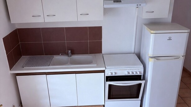 A compact kitchen with white cabinets, a built-in oven, and a refrigerator.