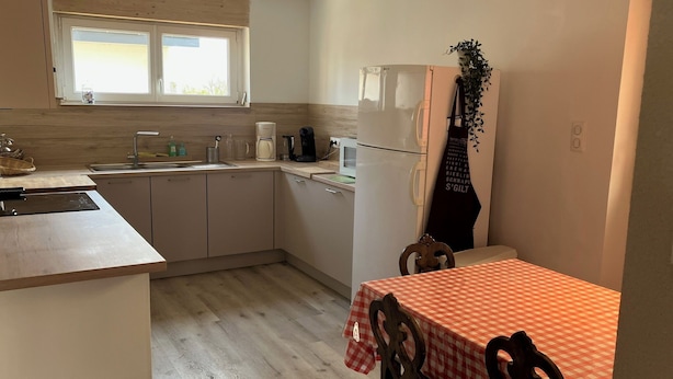 A compact kitchen with a sink, stove, and microwave. There is a dining table with a checkered tablecloth and chairs.