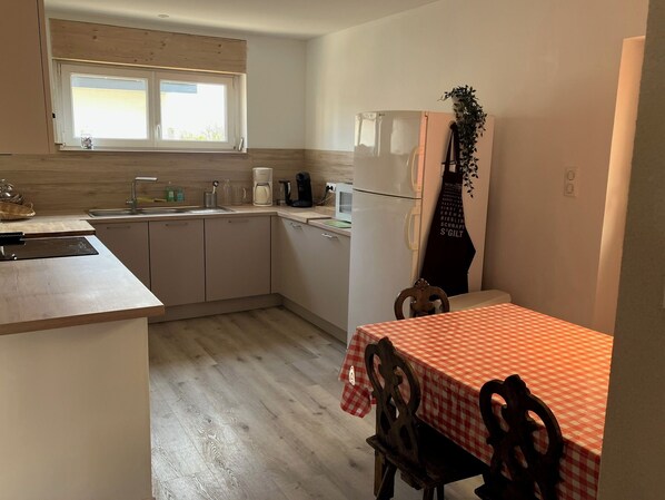 A compact kitchen with a sink, stove, and microwave. There is a dining table with a checkered tablecloth and chairs.