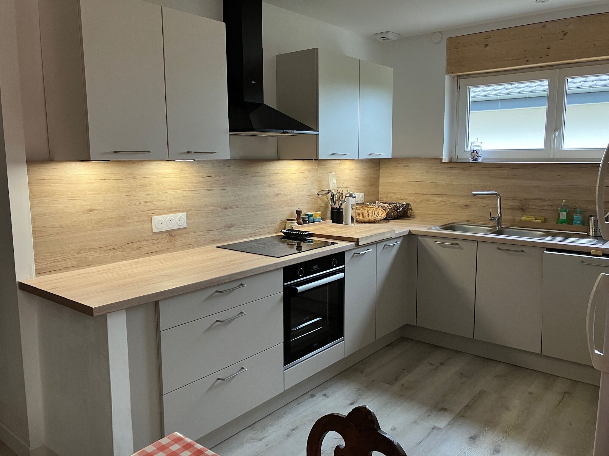 A modern kitchen with light wood cabinetry, a built-in oven, and a window above the sink.