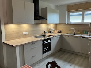 A modern kitchen with light wood cabinetry, a built-in oven, and a window above the sink.