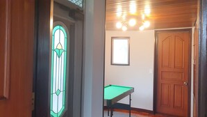 Een gang met een houten deur, een groene pooltafel en een glas-in-loodraam.
