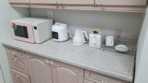 A kitchen with a microwave, coffee maker, kettle, toaster, and a mug rack.