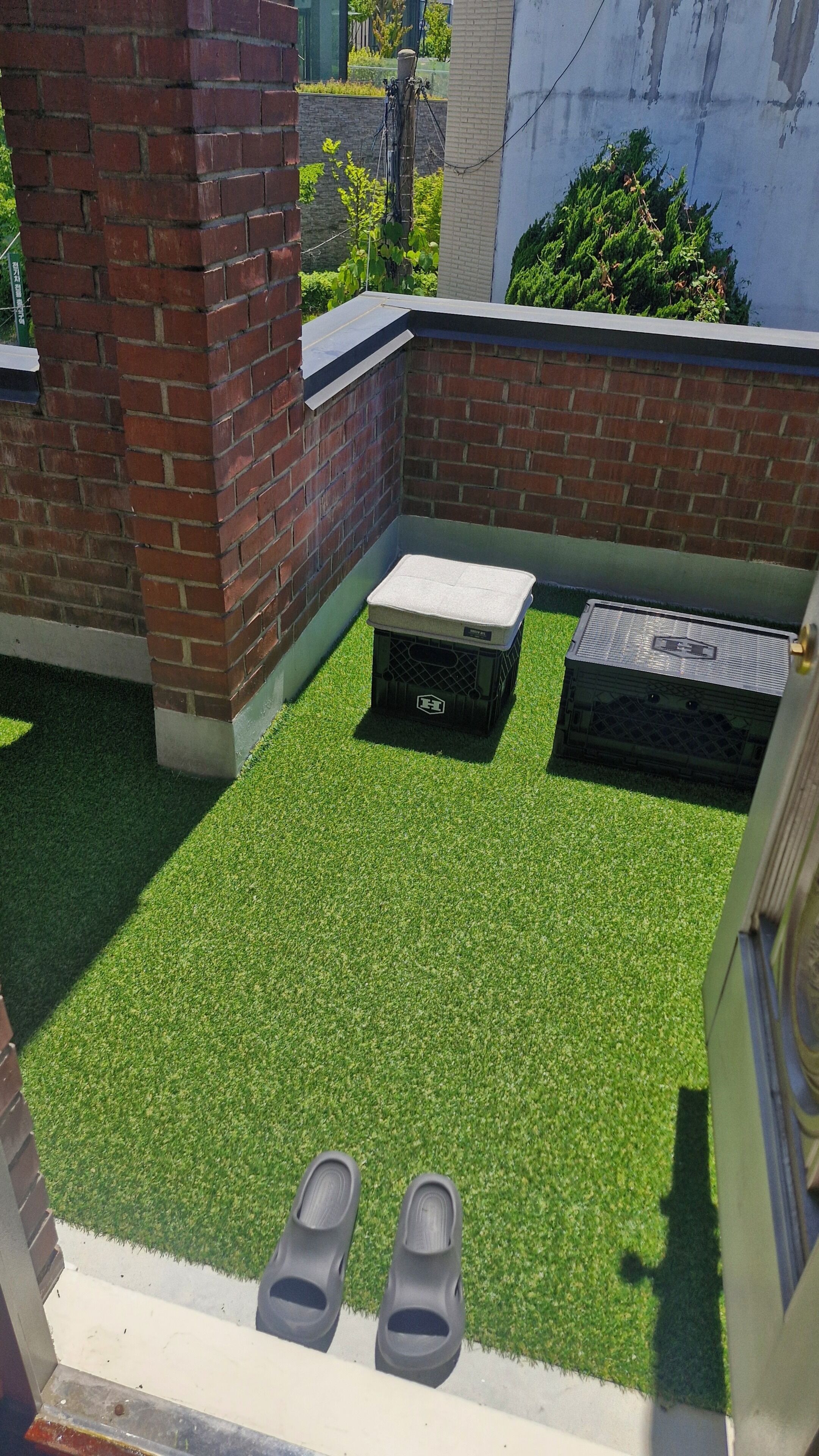 A rooftop patio with artificial grass, a brick wall, and a metal structure.