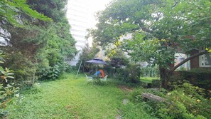 Un jardín exuberante con una pequeña mesa y sillas bajo un paraguas azul, rodeado de follaje denso y un muro de ladrillo.