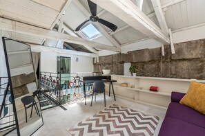 Ein Zimmer mit Deckenventilator, Schreibtisch, Stuhl, Sofa und einem Teppich mit Fischgrätenmuster.