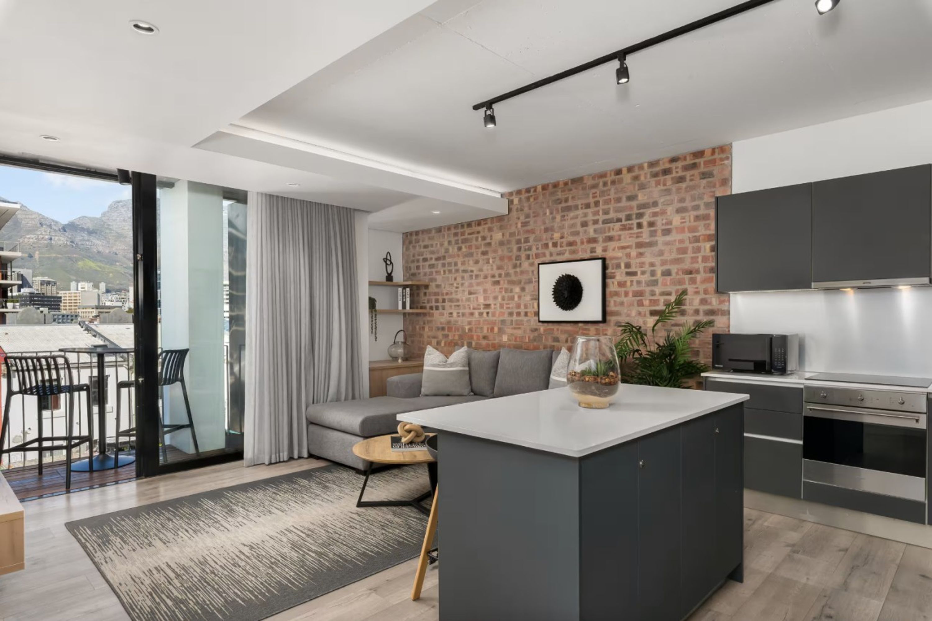 A modern kitchen with a brick wall, a dining area with a sofa, and a view of the city.