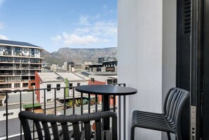 Ein Balkon mit Tisch und Stühlen, mit Blick auf eine Stadtlandschaft, einschließlich Gebäude und Berge in der Ferne.