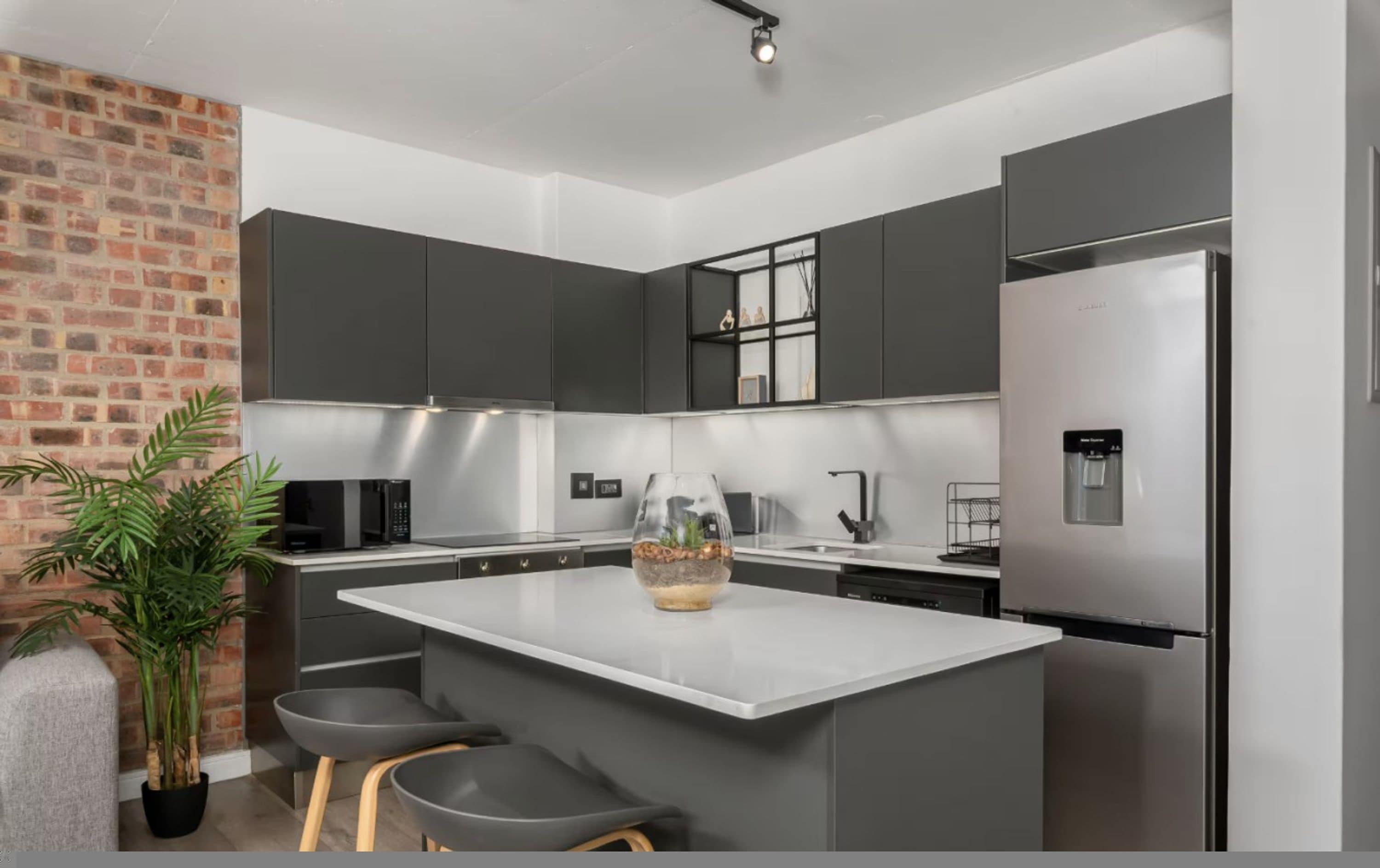 Cocina moderna con armarios grises, una isla central, un refrigerador y una planta en maceta.
