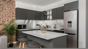 A modern kitchen with grey cabinets, a central island, a refrigerator, and a potted plant. - Stylish 1 Bed Secure Spacious Mountain Views (Cape Town)