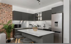 Eine moderne Küche mit grauen Schränken, einer zentralen Kochinsel, einem Kühlschrank und einem Blumentopf.