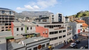 A multi-story building with a rooftop terrace, a prominent sign, and a mountain in the background. - Stylish 1 Bed Secure Spacious Mountain Views (Cape Town)