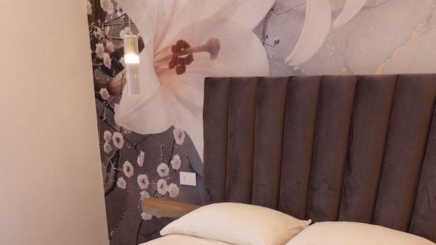 Una cama bien hecha con una toalla blanca doblada, un cabecero de madera y una decoración floral en la pared.