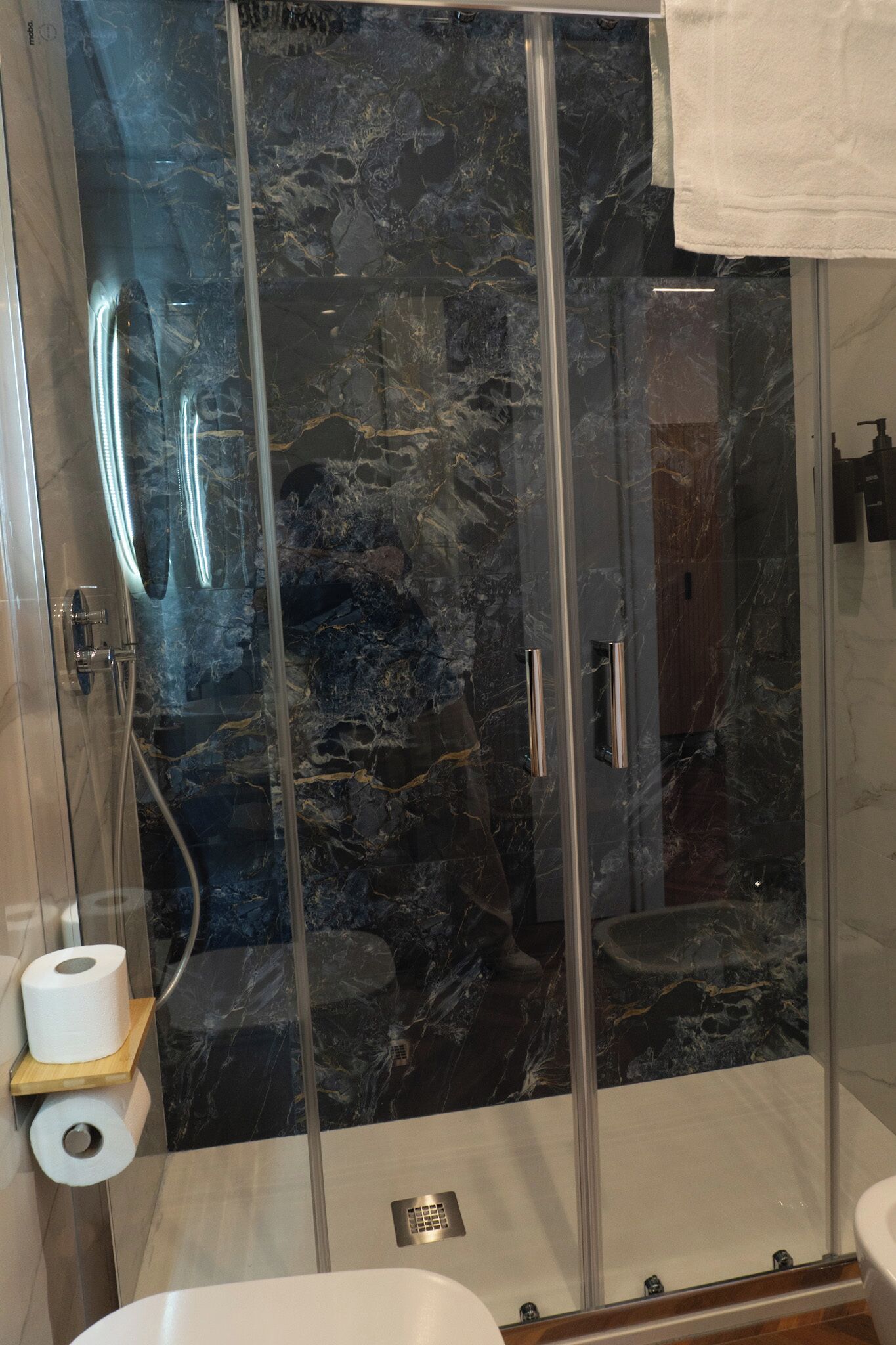 Une salle de bain moderne avec une douche à parois de verre, des murs en marbre et un lavabo blanc.