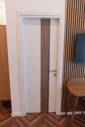 Eine geschlossene Tür mit einer vertikalen Holzplatte, ein kleiner Tisch mit einem Stuhl und eine Wand mit vertikalen Holzleisten.