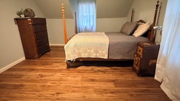 A bedroom with a wooden floor, a bed with a patterned bedspread, a dresser, and a ceiling fan.