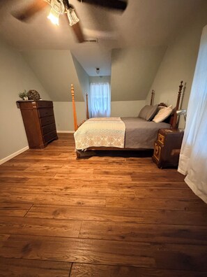 Ein Schlafzimmer mit Holzboden, einem Bett mit gemustertem Überwurf, einem Schminktisch und einem Deckenventilator.