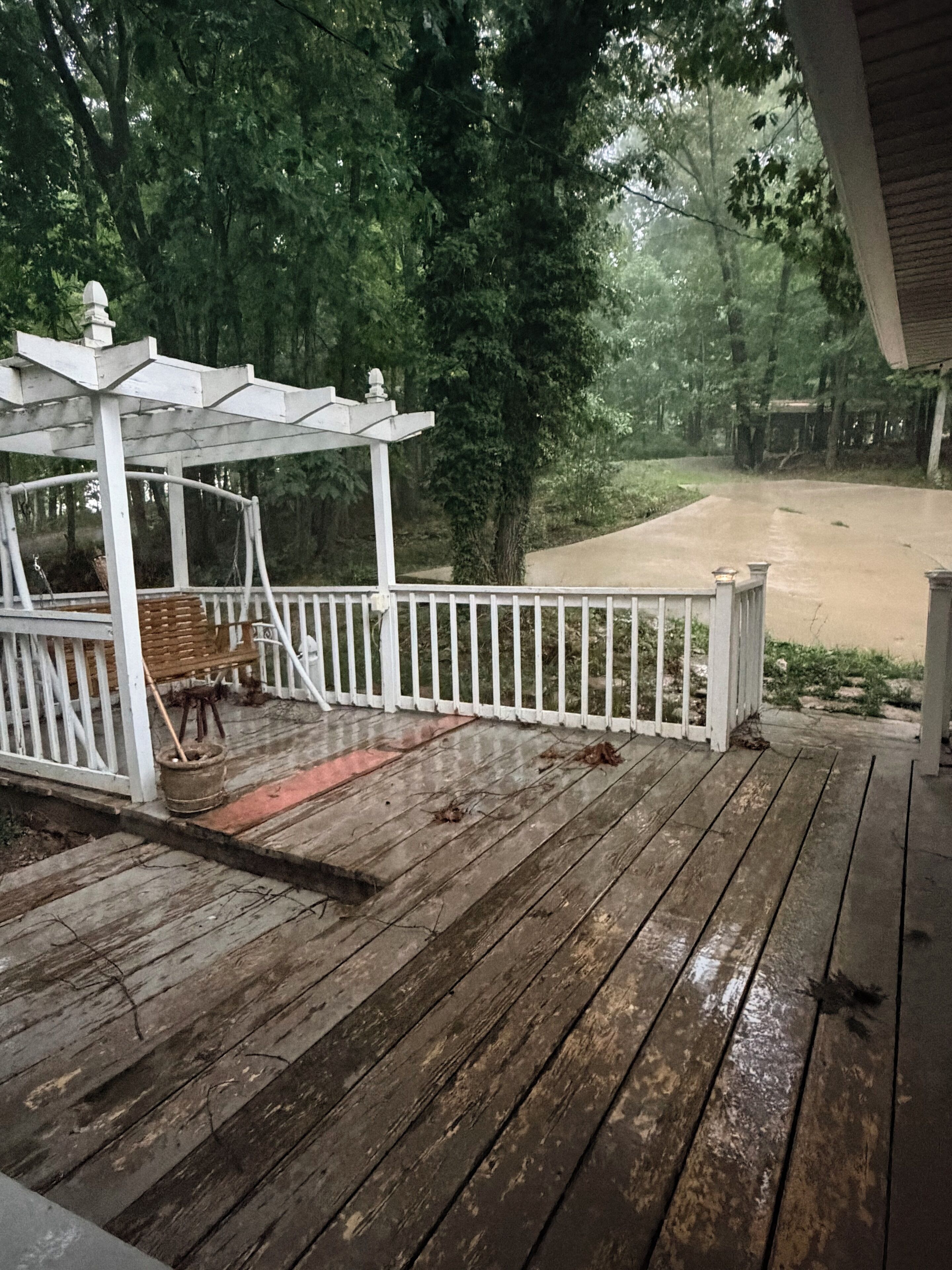A wooden deck with a white railing, a covered seating area, and a view of a forested area.