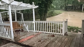 A wooden deck with a white railing, a covered seating area, and a view of a forested area.