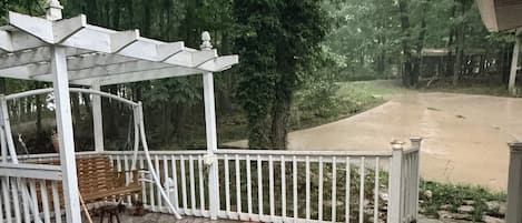 A wooden deck with a white railing, a covered seating area, and a view of a forested area.