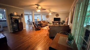 A spacious living room with hardwood floors, a dining area, and a kitchen visible in the background.