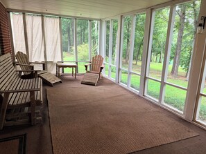 Una veranda con ampie finestre, un muro in mattoni e poltrone Adirondack in legno.