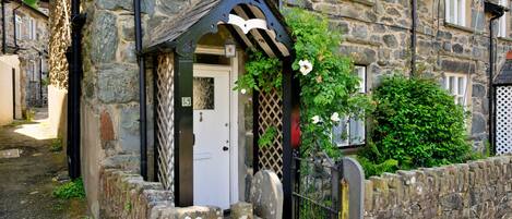 A stone building with a white door, a small porch with a wooden railing, and a stone wall.