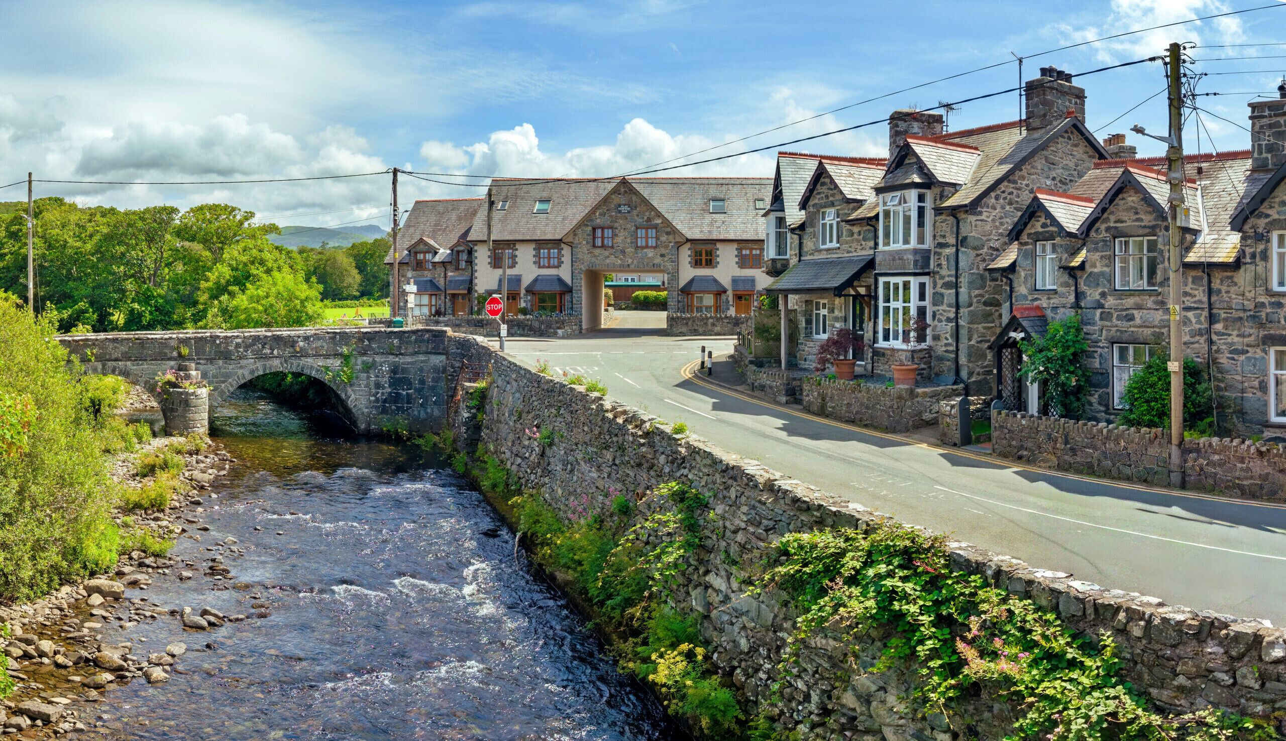 Un pont de pierre enjambant une rivière, un bâtiment en pierre avec une enseigne, et une route menant à ce bâtiment.