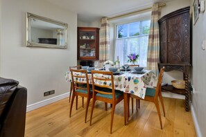 Ein Essbereich mit einem Tisch für vier Personen, Holzstühle, eine Vitrine mit Glastüren und ein Fenster mit Vorhängen.