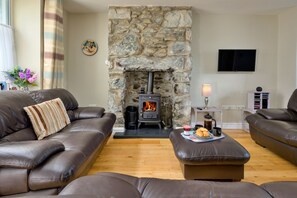A living room with a stone fireplace, leather sofas, a coffee table with pastries, and a flat-screen TV on the wall. - Artro View (Llanbedr)