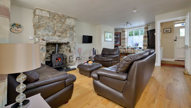 A living room with a stone fireplace, leather sofas, a television, and a dining area with a table and chairs. - Artro View (Llanbedr)