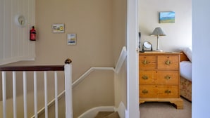 A staircase with a white railing, a wooden nightstand with drawers, a lamp, and a framed picture on the wall. - Artro View (Llanbedr)