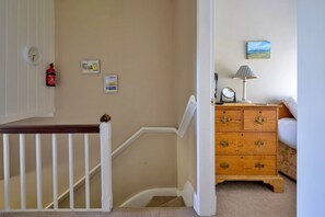 A staircase with a white railing, a wooden nightstand with drawers, a lamp, and a framed picture on the wall. - Artro View (Llanbedr)
