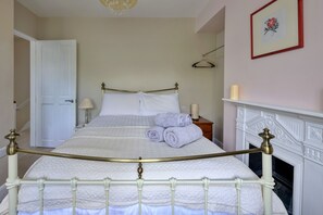 Et soveværelse med en seng, en hvid dør, et sengebord med en lampe, en pejs og et billede i ramme på væggen.