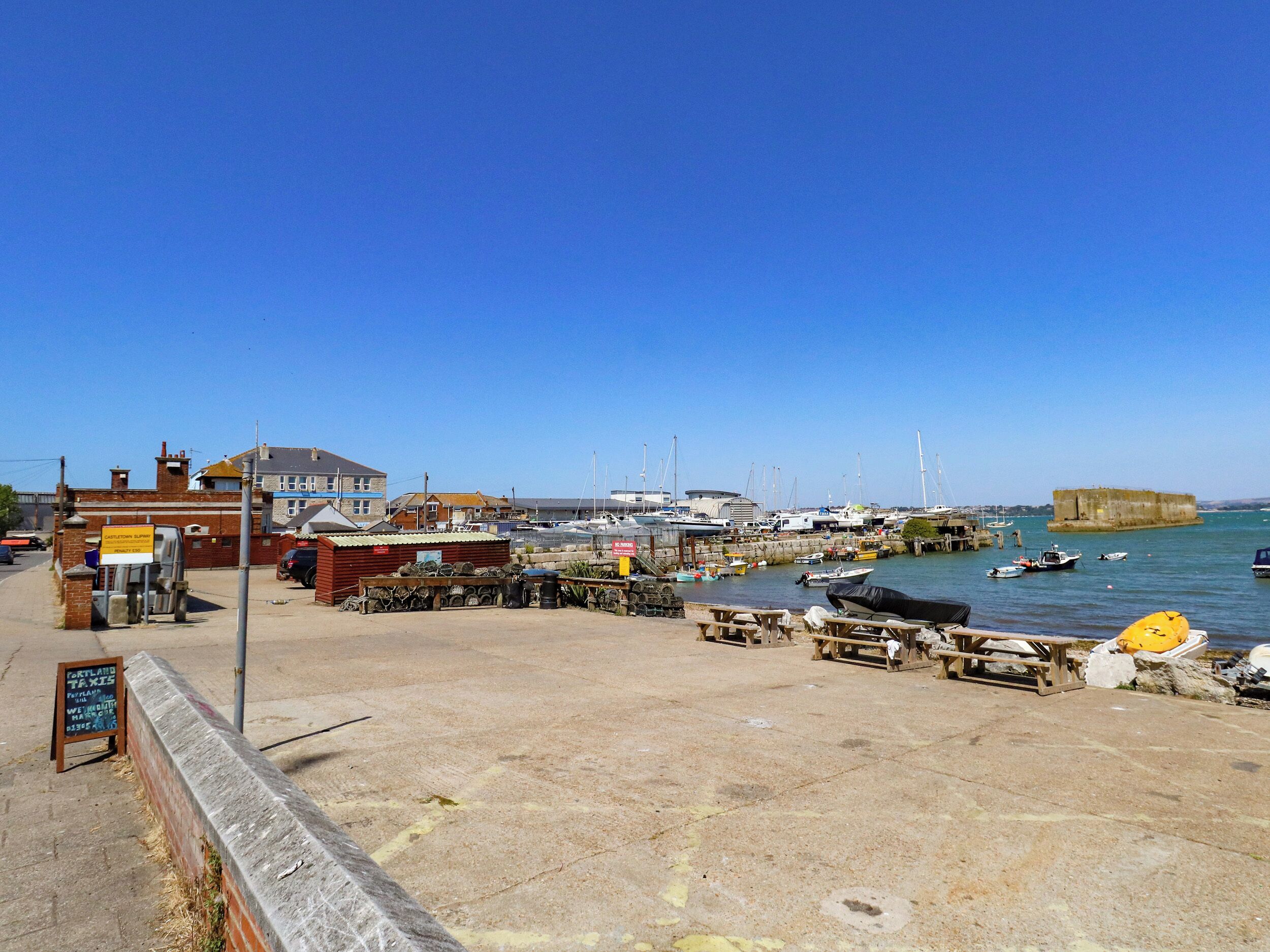 A coastal marina with boats, a stone wall, and a signboard.