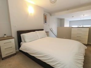 A bedroom with a bed, bedside tables, a dresser, and a wall-mounted light fixture.