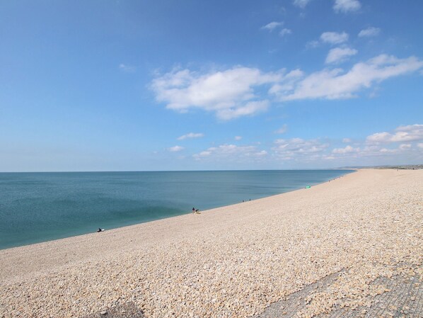 A wide, pebbled beach with a clear sky and calm sea.