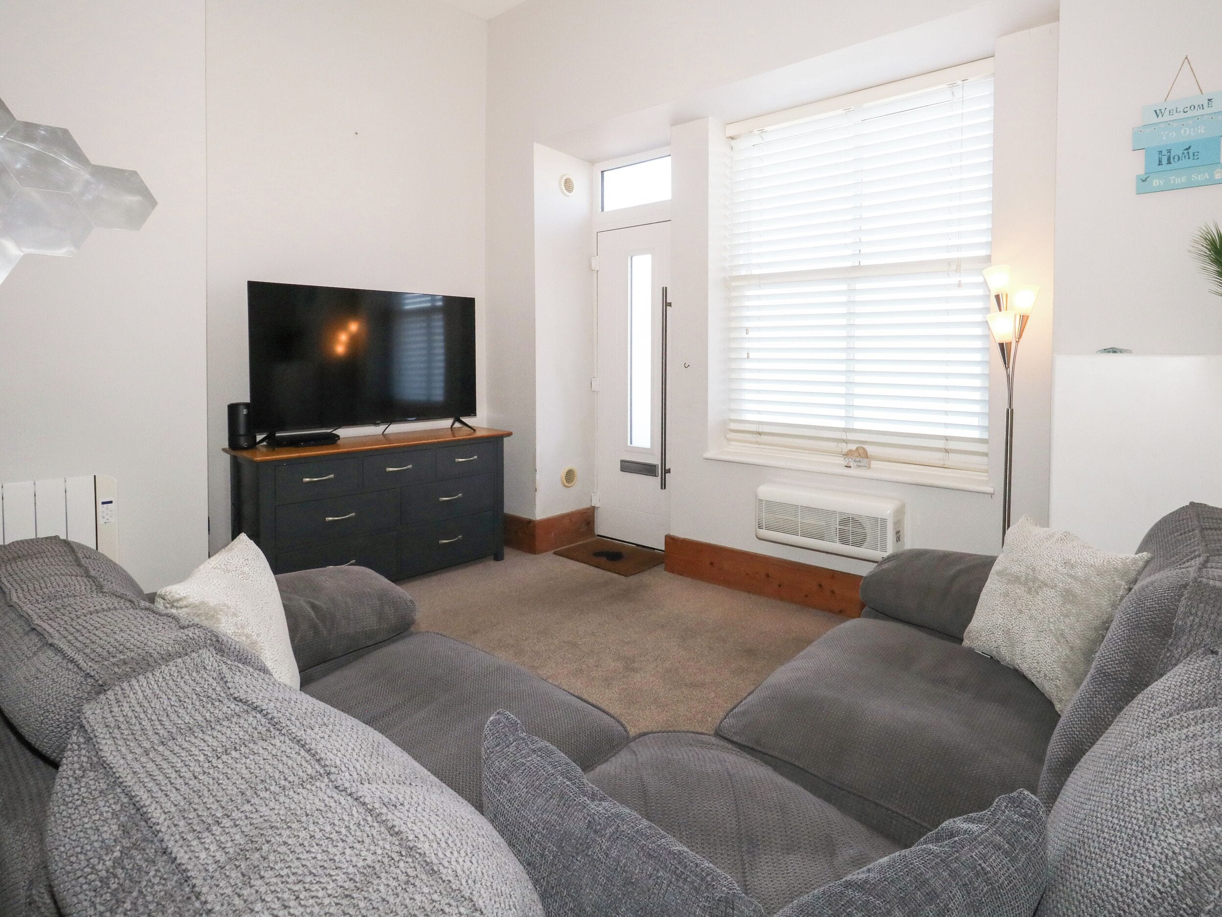 Una sala de estar con televisor, muebles oscuros, una puerta blanca y una ventana con persianas.